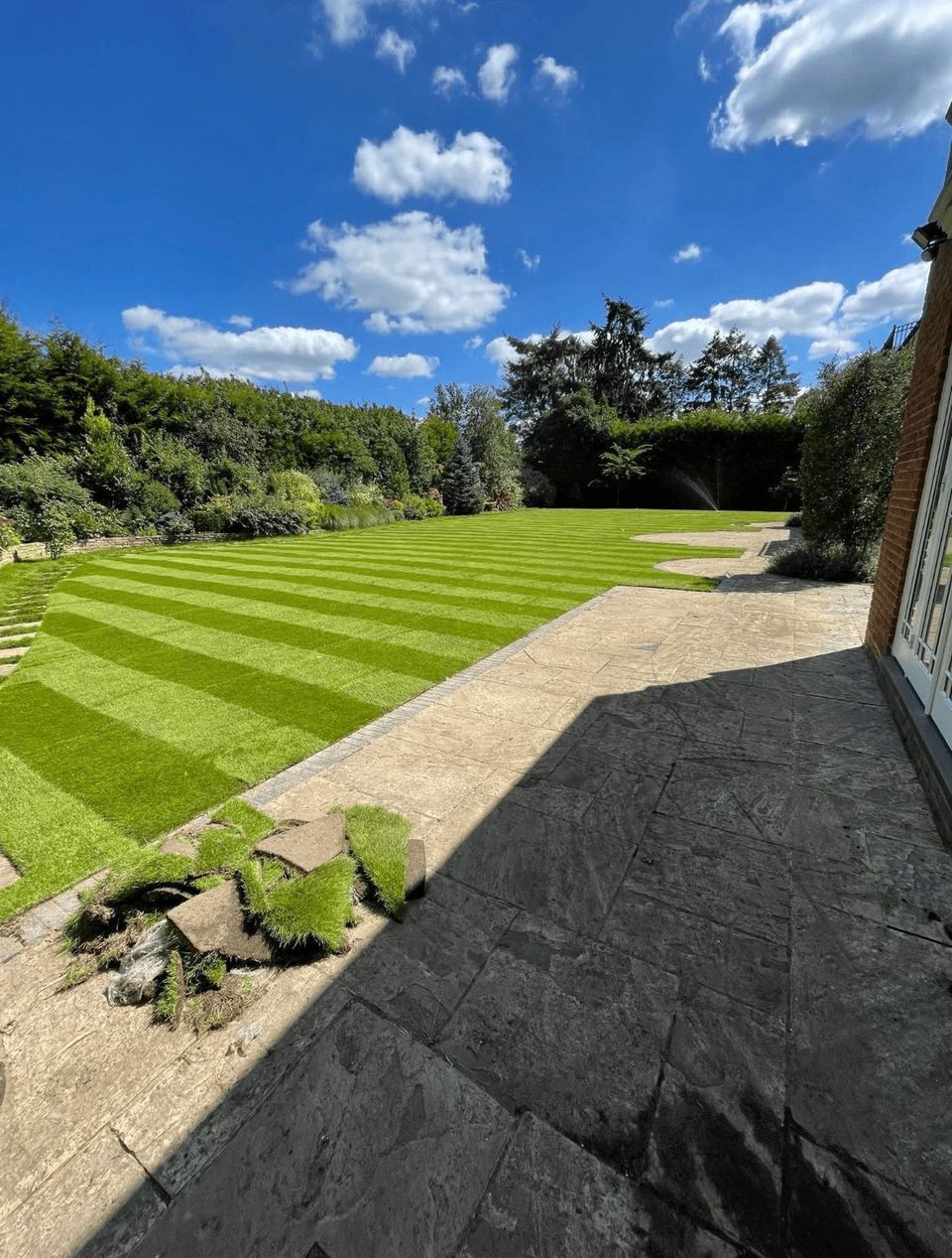 Freshly laid striped lawn next to a paved patio on a sunny day