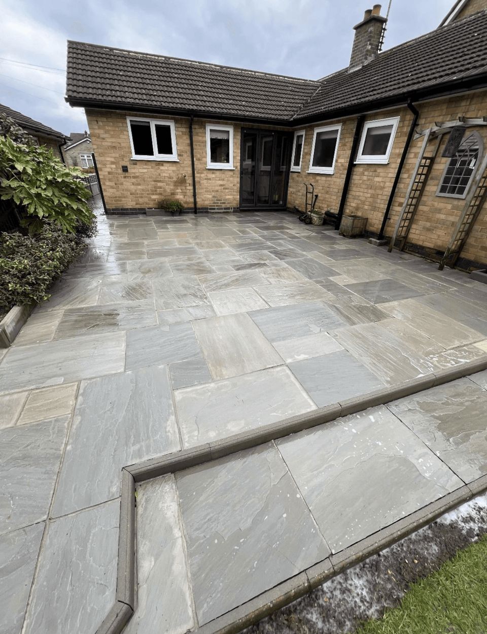 Clean grey sandstone patio laid behind a brick bungalow